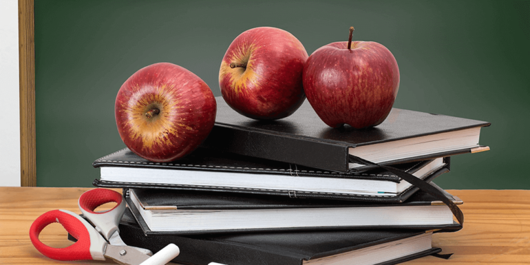 Three apples on top of a stack of books.